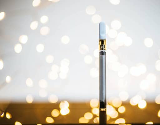Silver cannabis vape pen on wooden table with sparks flying around the background