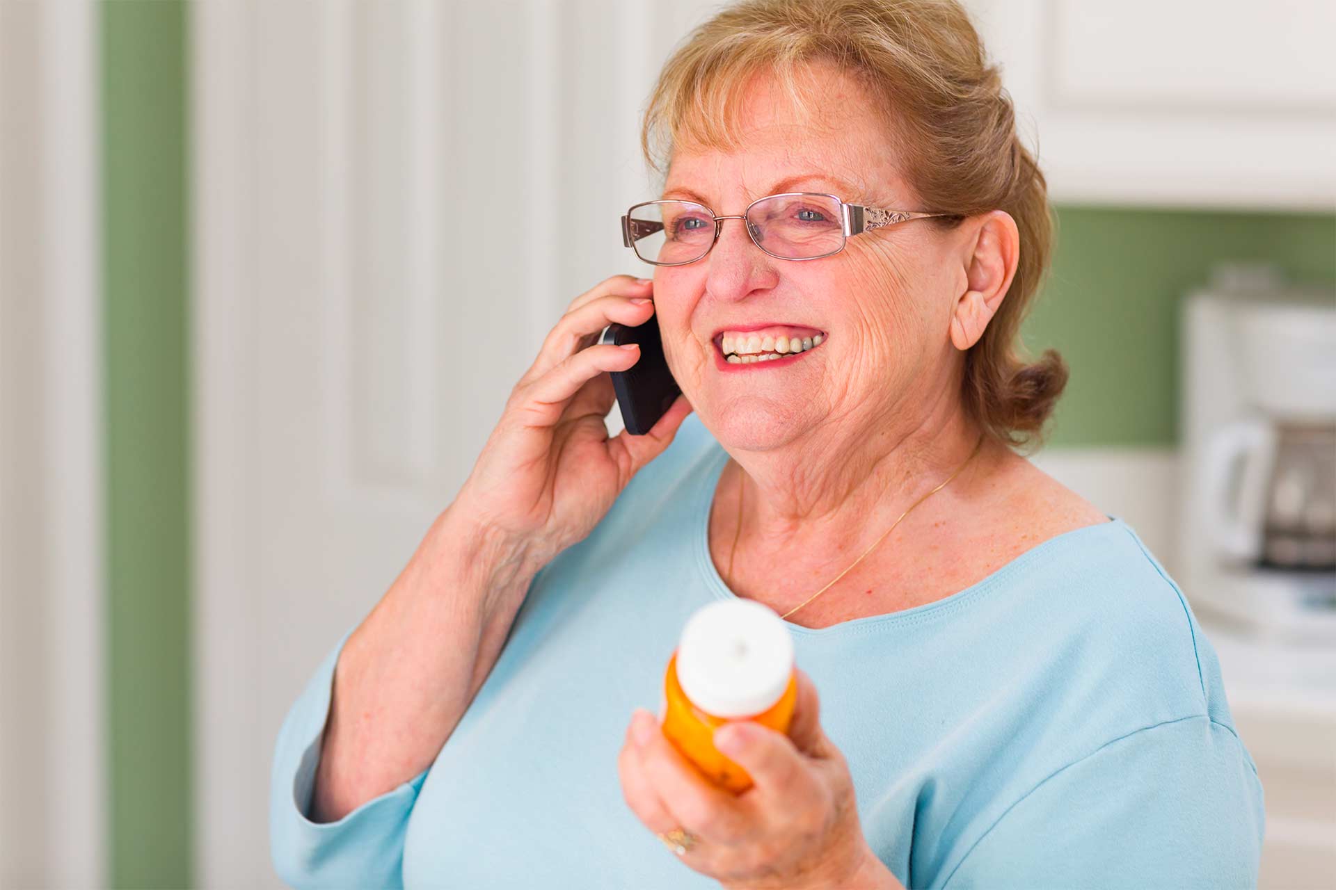 Smiling senior woman on phone holding prescription bottle, asking about drug interactions with cannabis.