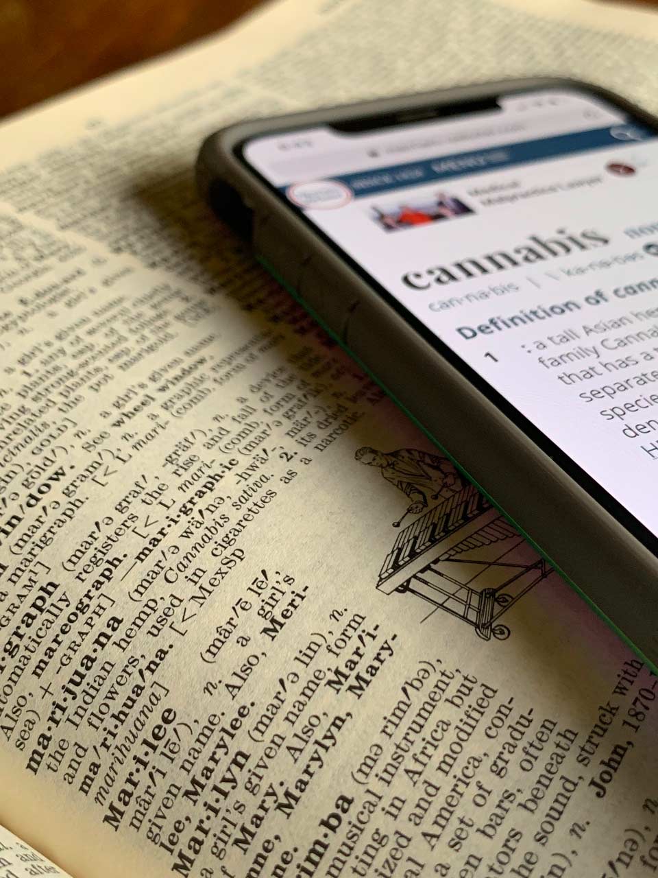 Dictionary book page with smartphone placed on top, showing dictionary definition of cannabis. Photo by Margo Amala/Unsplash