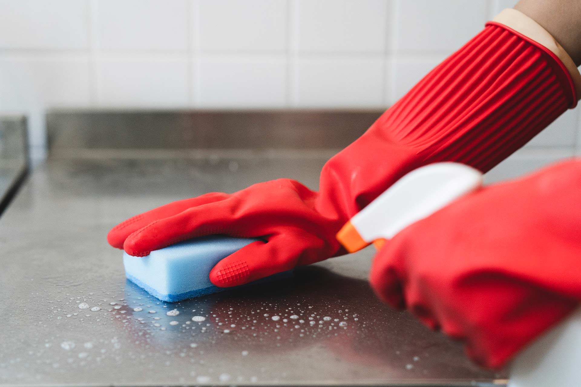 Close up of showing hands with rubber cleaning gloves on, spraying disinfectant and cleaning metal table top.