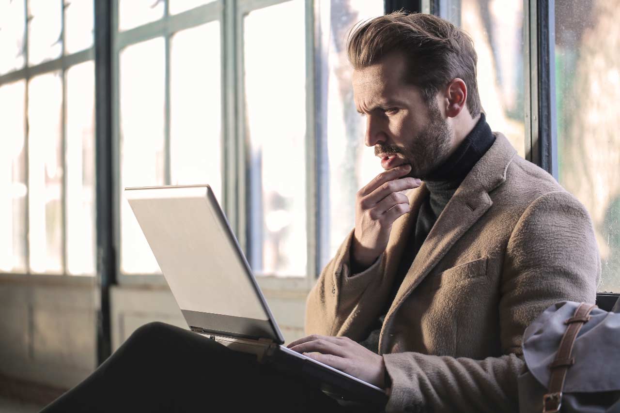 Sitting man looks at laptop computer screen with puzzled expression and hand on chin. Photo by Bruce Mars/Unsplash