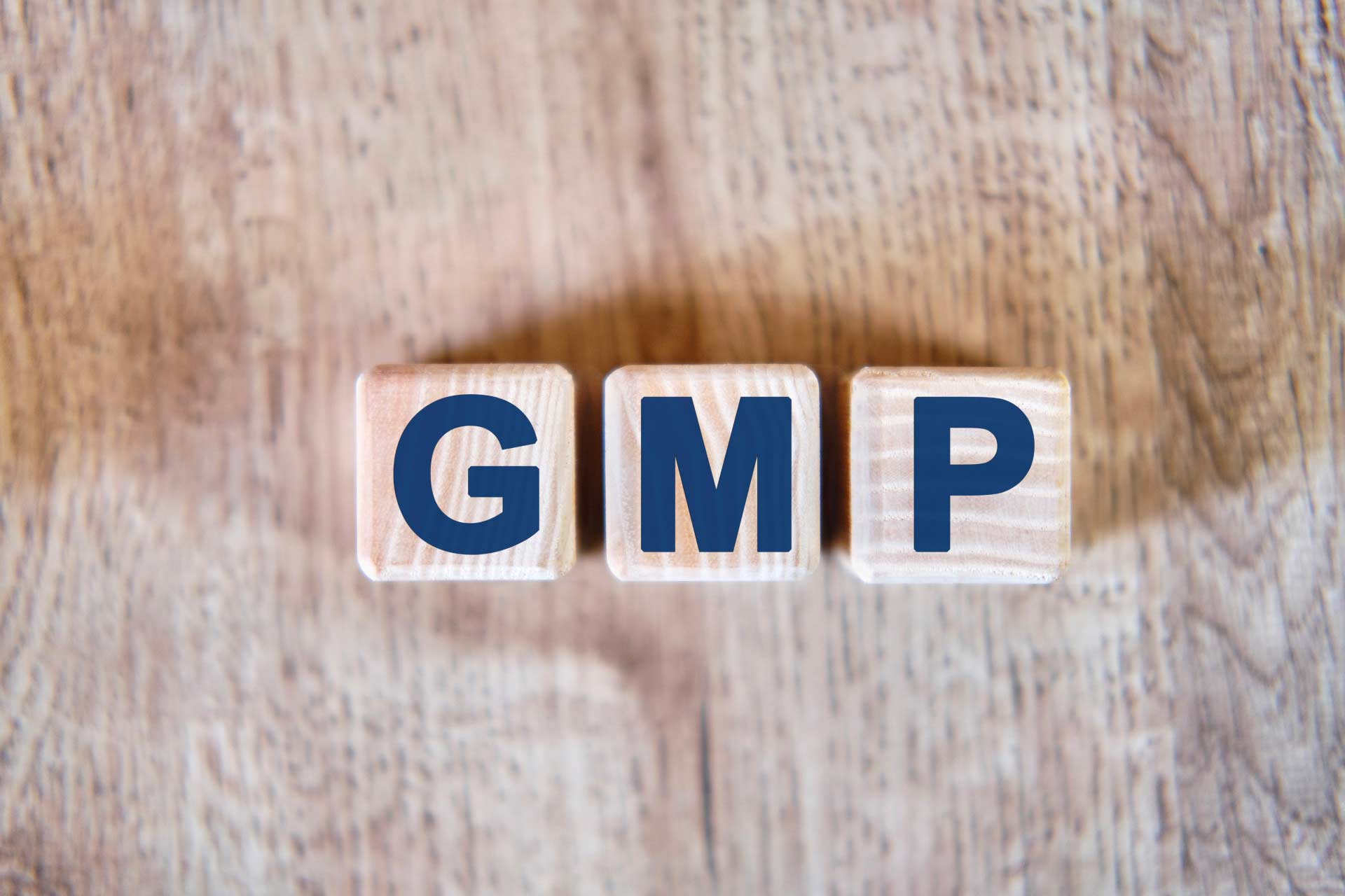 Wood letter dice with “G-M-P” standing for Good Manufacturing Practices, which Wana Brands follows.