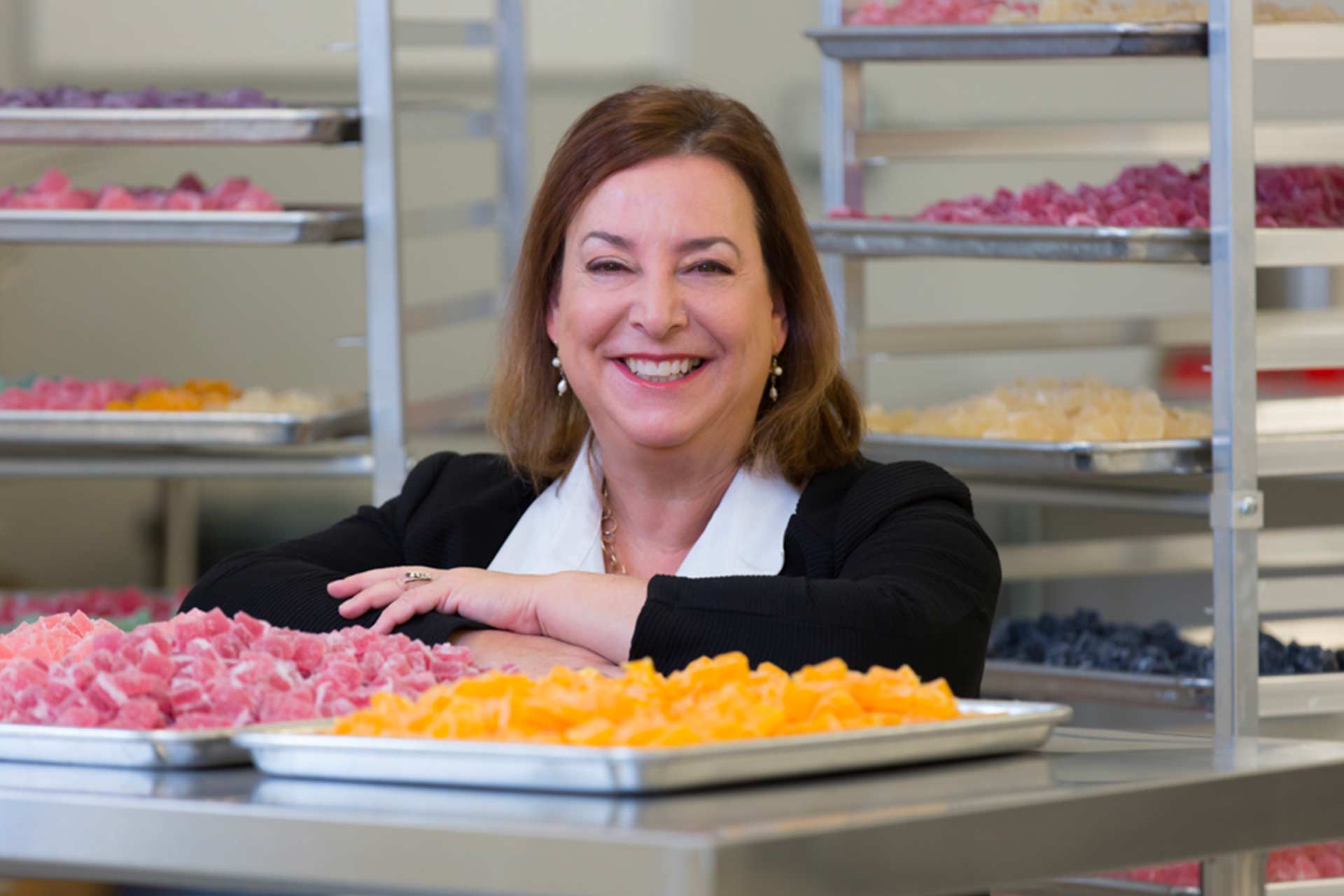 Nancy standing smiling in Wana Brands production facility, with trays of cannabis gummies on the table in front of her.