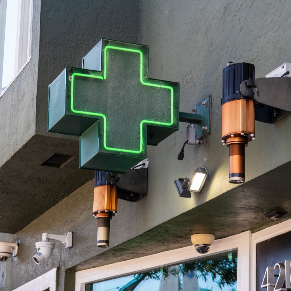 Green neon cross outside of a medical marijuana dispensary, indicating that cannabis is an essential need and is open for business.