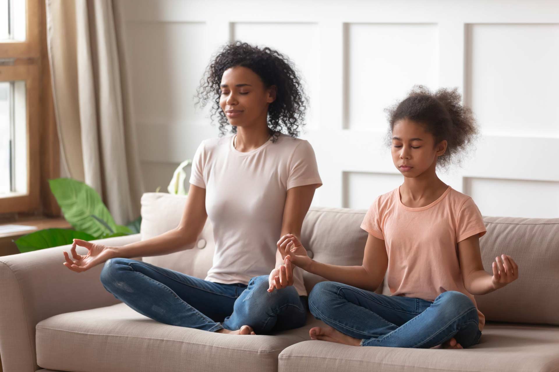 An African-American mother and her daughter doing yoga together, sitting in easy pose with eyes closed, representing other wellness strategies.