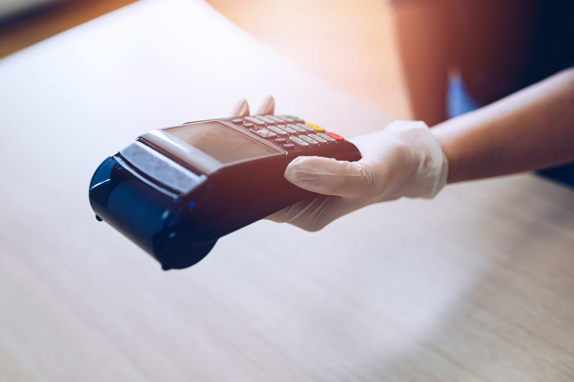 Portable credit card machine held in a gloved hand, showing precautions marijuana dispensaries take to keep customers and employees safe.