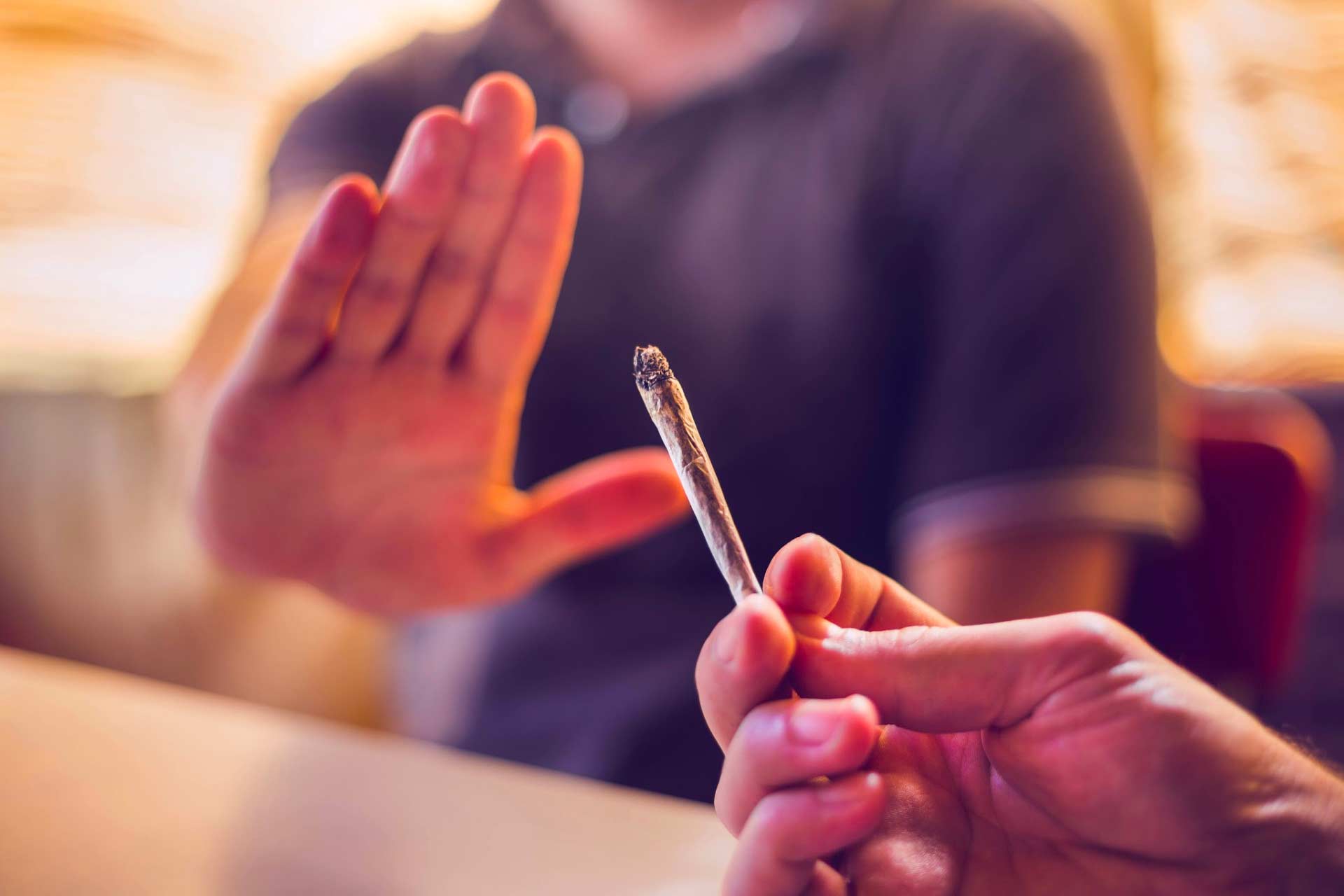 Close-up of hand holding joint offering it to another person, with the other person’s hand up declining, choosing other cannabis consumption methods instead.