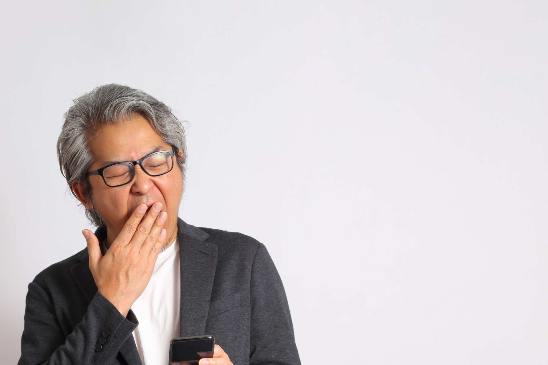 Older Asian man yawning while looking at his phone.