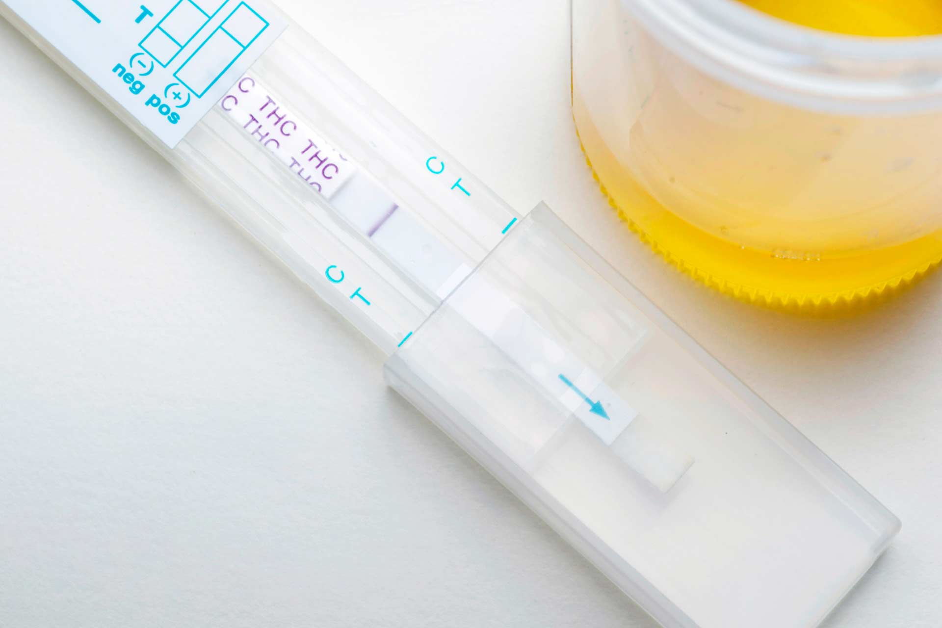 Home drug test for THC, with urine specimen cup beside it.