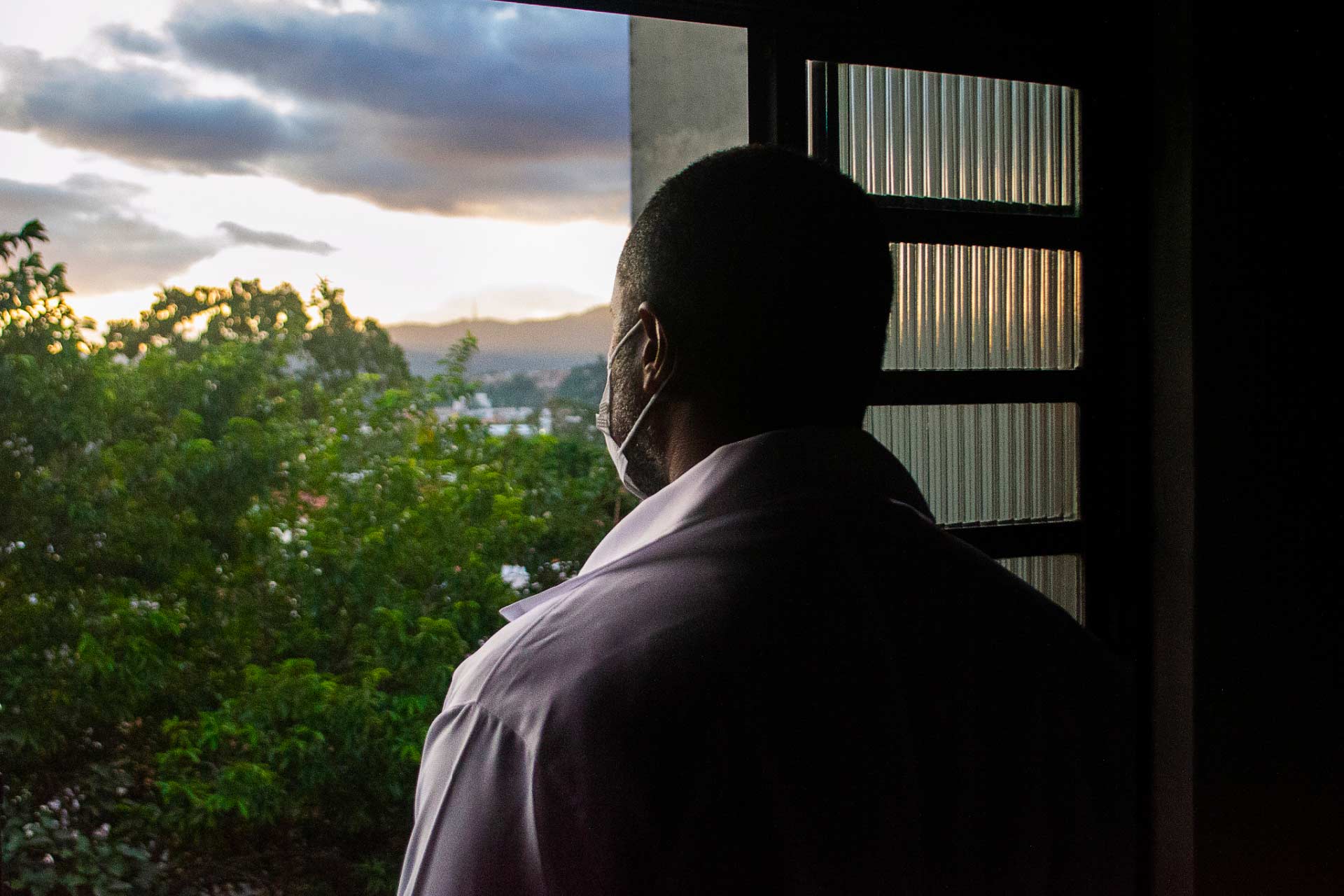 A Black veteran stares out a window from a darkened room.