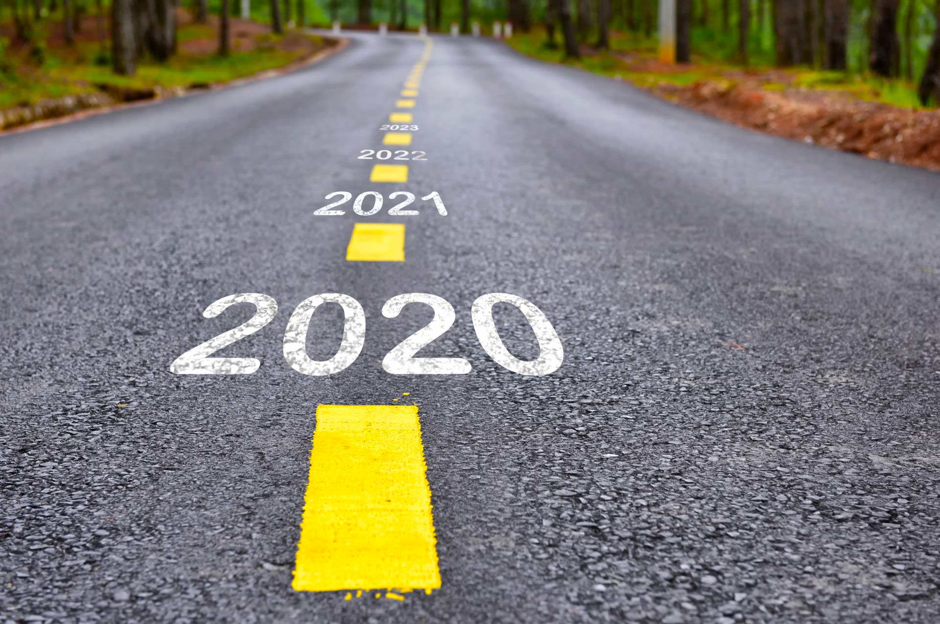 Asphalt road through forest with the years “2020,” “2021,” etc. stretching ahead toward the future.
