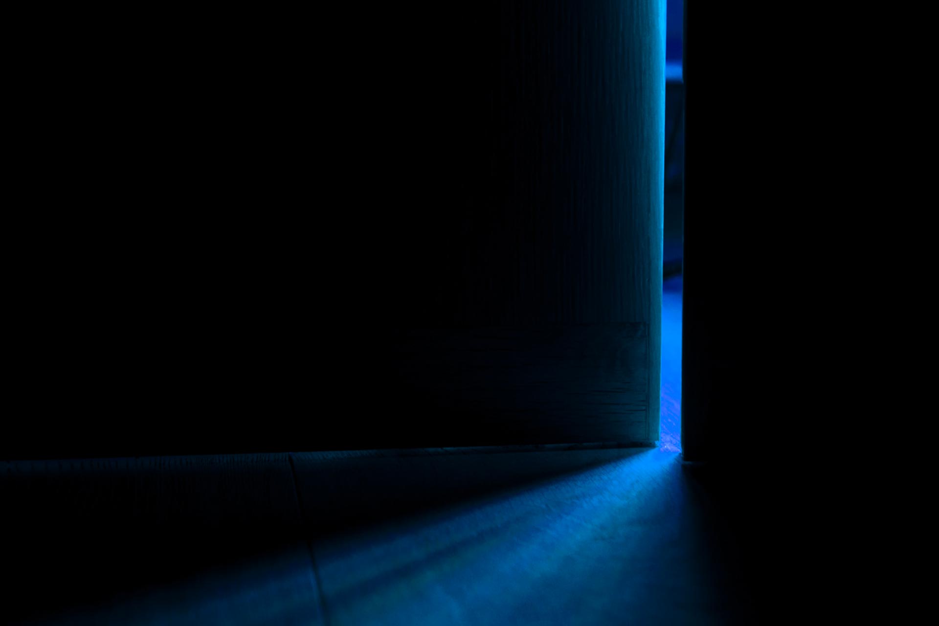 Dark room with door cracked open, letting in blue light, indicating fear and isolation