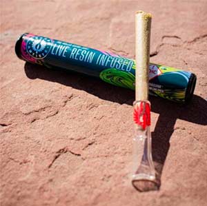 Escape Artists Live Resin infused preroll joint with a glass tip, sitting on top of colorful packaging