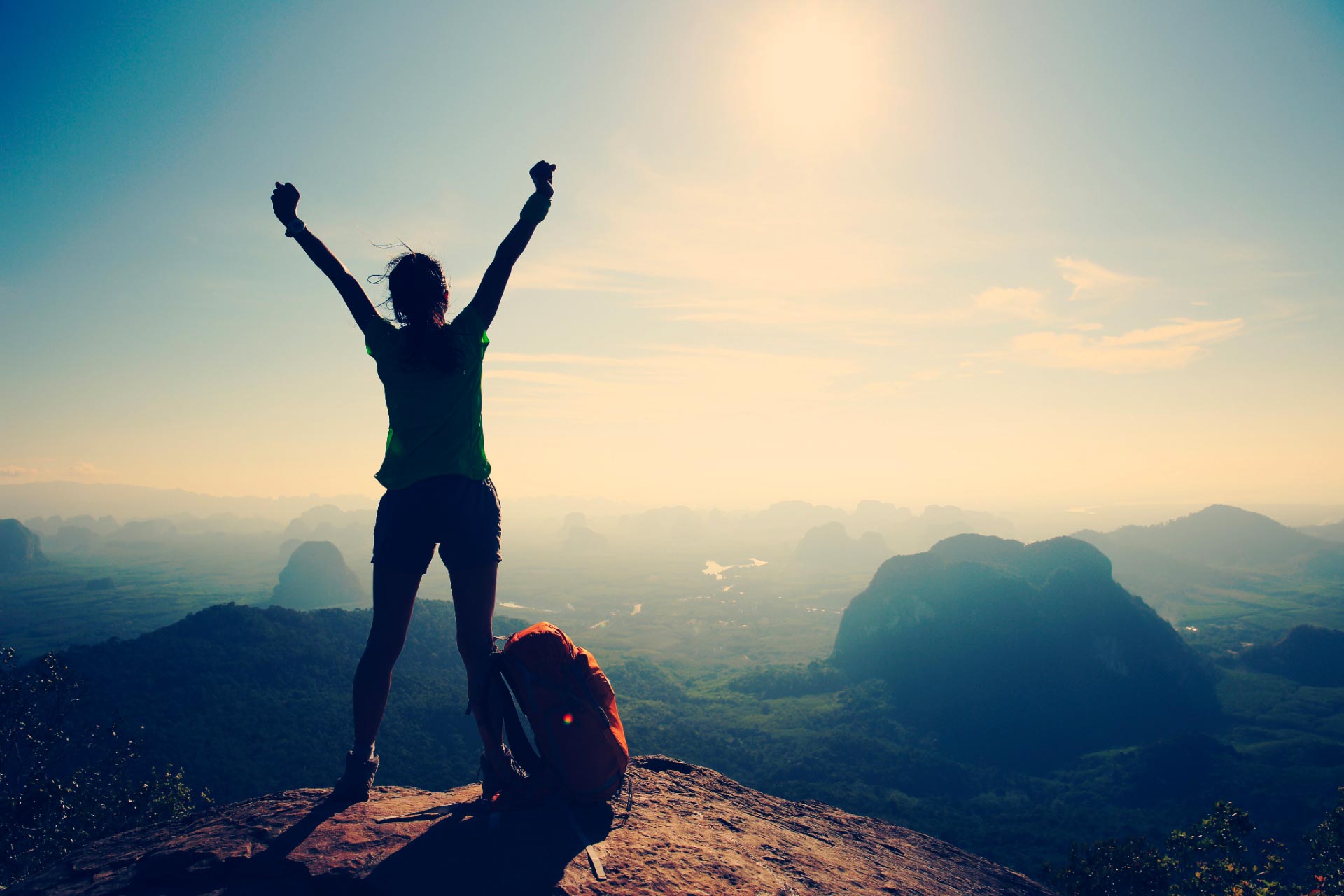 Woman standing on top of mountain peak, arms raised in victory