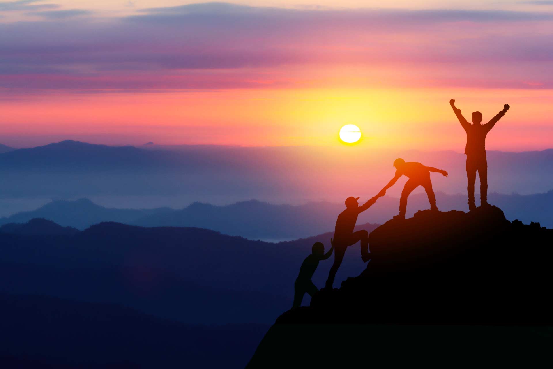 Silhouette of four people summiting a peak at sunrise.
