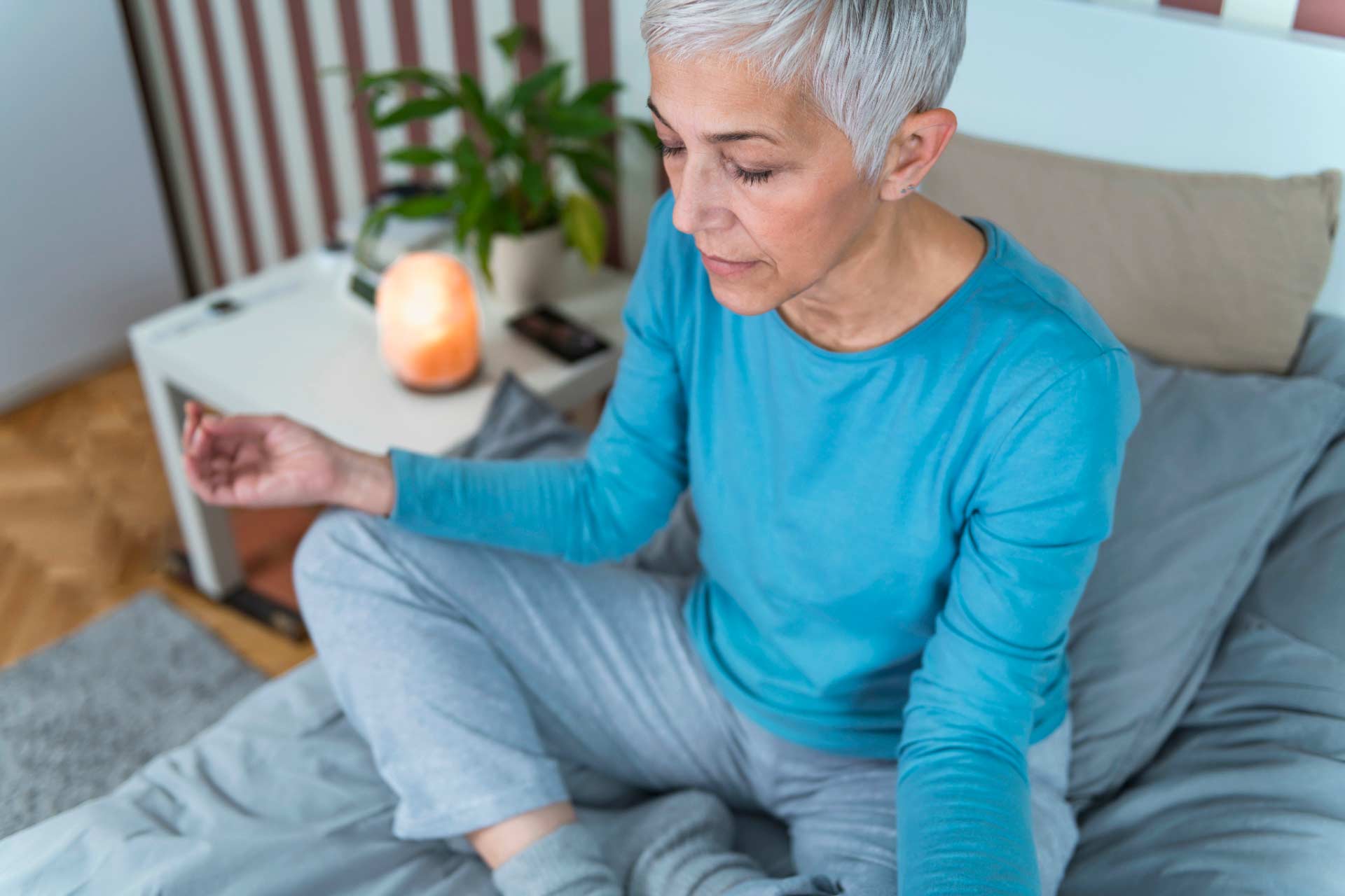 Older woman sitting on her bed in a yoga pose, meditating.