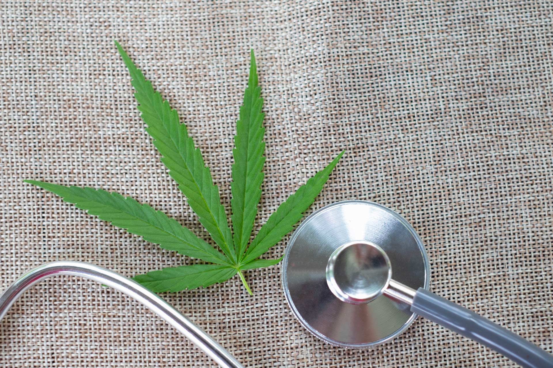 Nurse’s stethoscope and a cannabis leaf on natural hemp fabric background