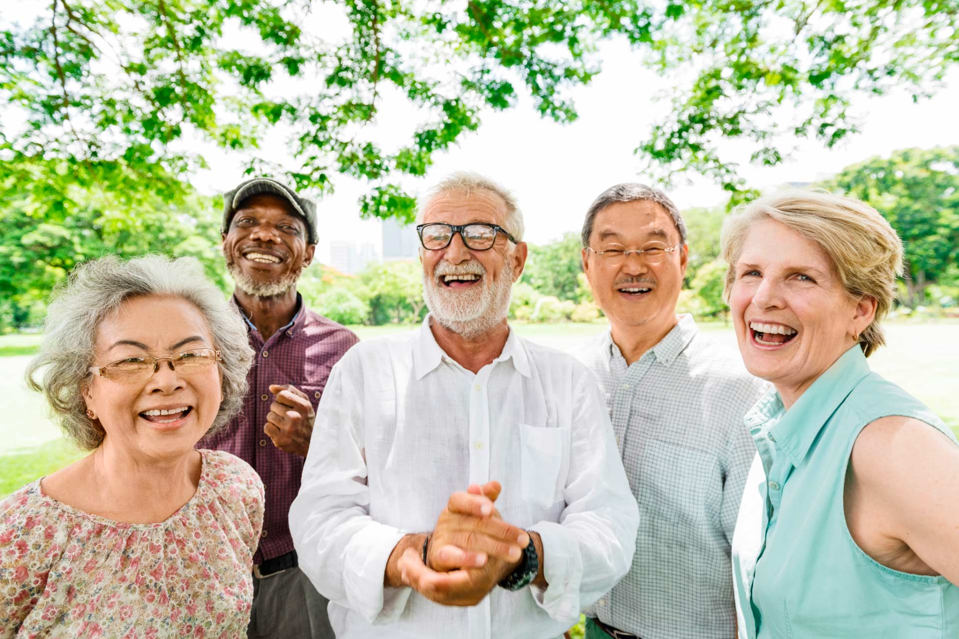 Five diverse older adults at a park on sunny day, smiling and socializing.