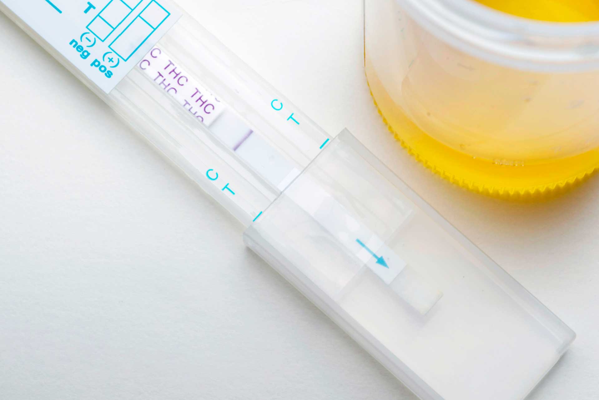 THC drug test strip beside a urine sample in a cup.