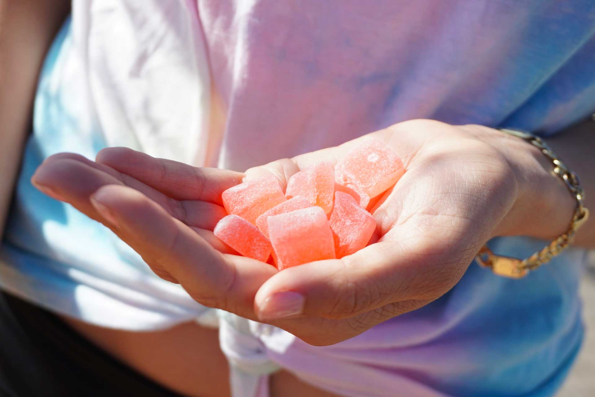 Young woman’s hand holding peach-colored Delta-8 gummies.
