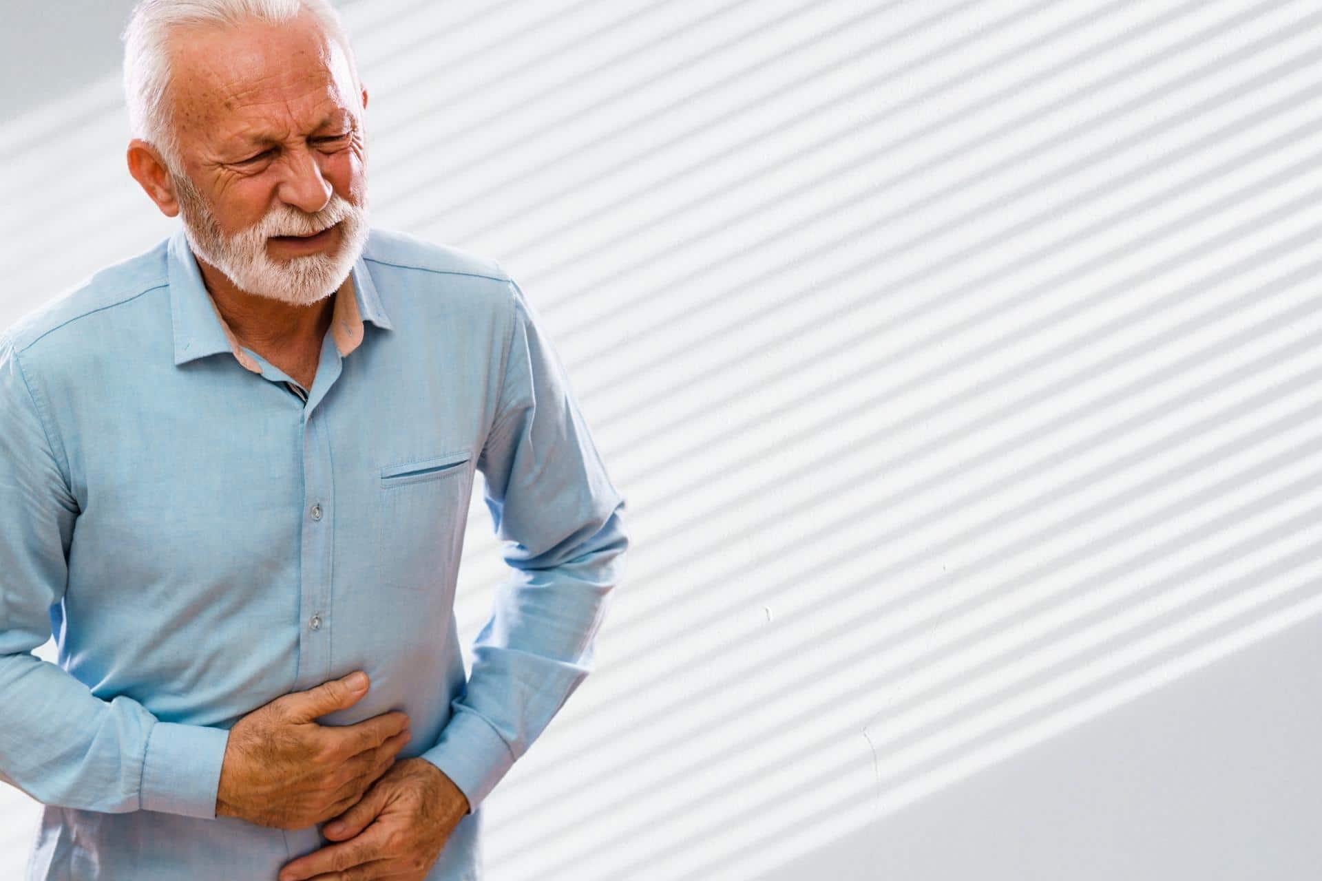 Older white man holding stomach and grimacing due to nausea from cannabinoid hyperemesis syndrome (CHS).