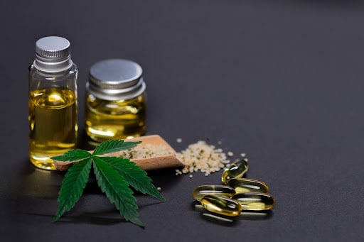 Cannabis oil in jars with cannabis oil capsules next to cannabis leaf on dark background