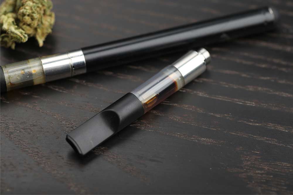 Cannabis vape cartridge filled with cannabis extract in front of a vape pen with a 510-threaded battery.