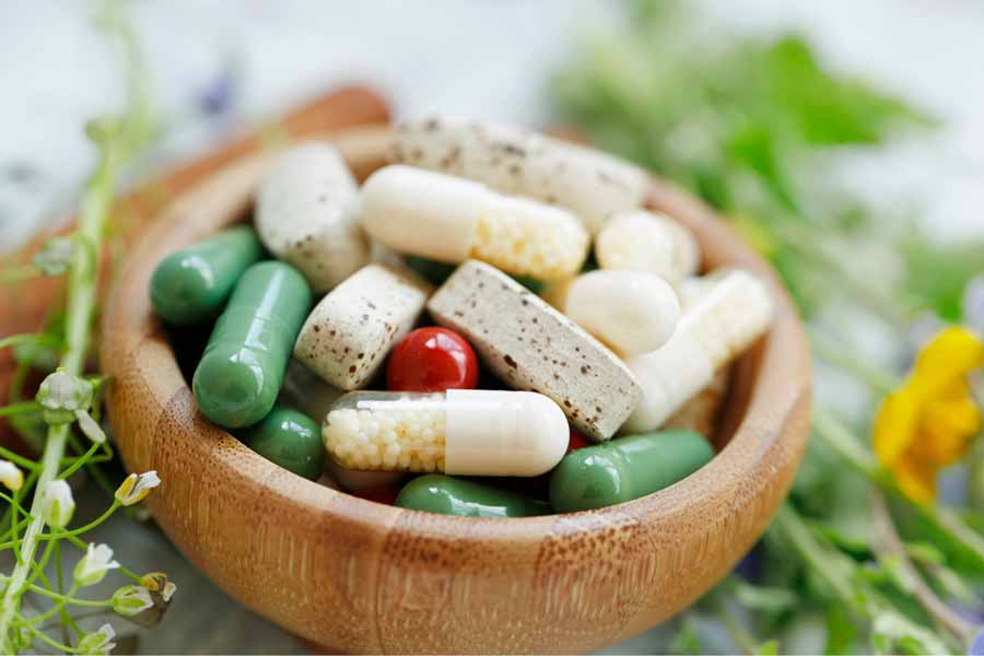 Pills and capsules in a wooden bowl surrounded by beneficial herbs that interact with the ECS