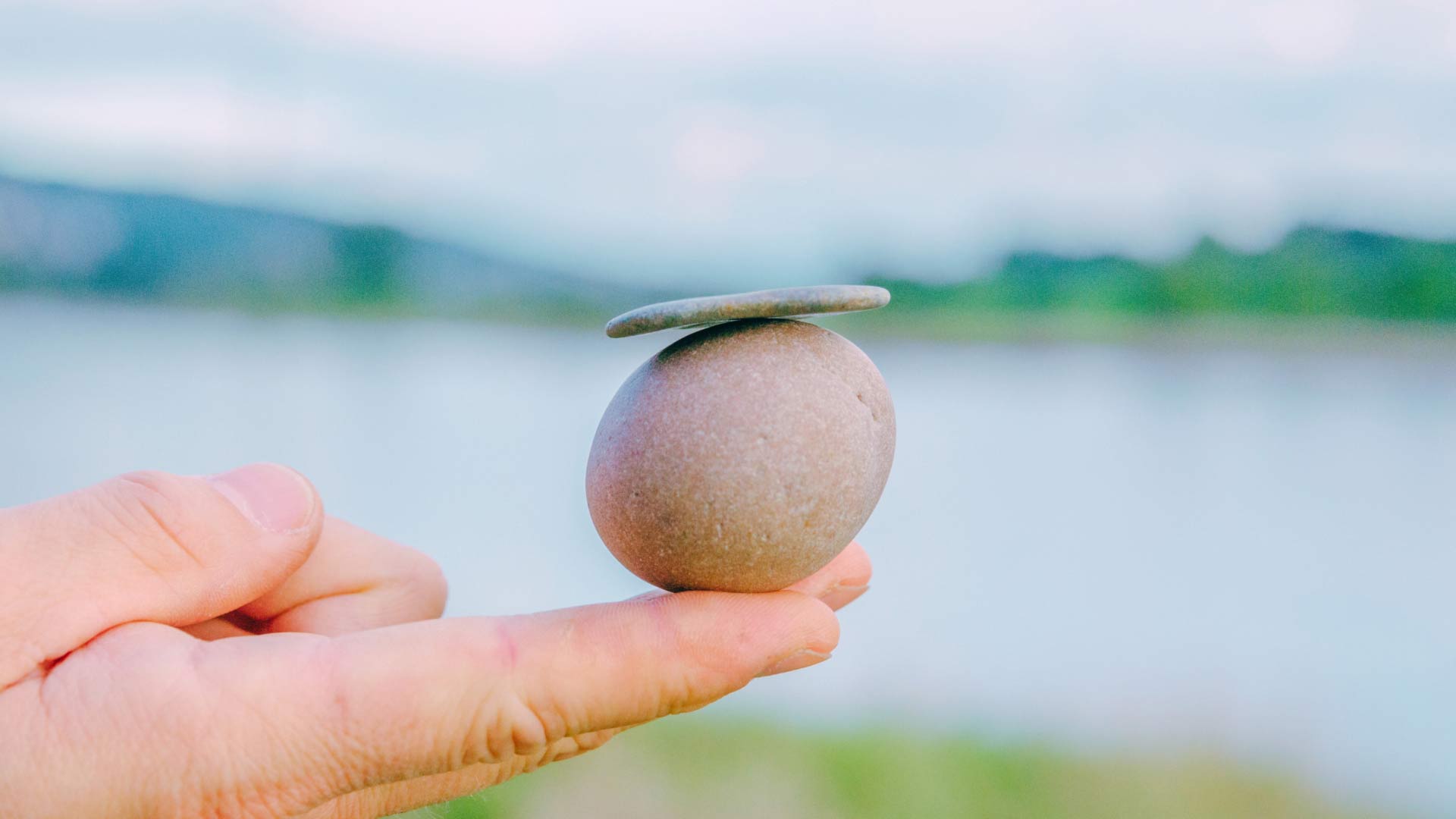Hand balancing rocks in front of lake, signifying the best balance of THC and CBD