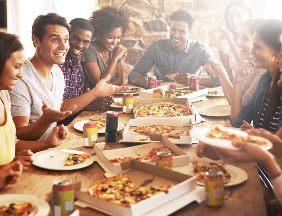 Group of friends around a table, laughing and enjoying cannabis spritzers and pizza.