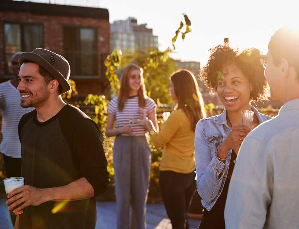 Diverse set of friends having a cheerful summer rooftop party which includes THC-infused beverages.